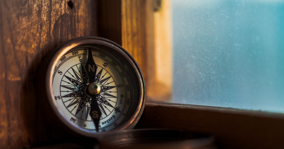 A brass compass resting on a wooden windowsill, with daylight behind it