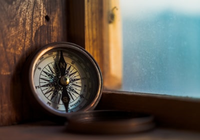 A brass compass resting on a wooden windowsill, with daylight behind it
