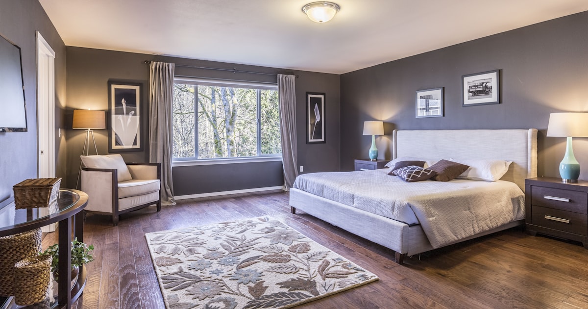 A large bedroom with the bed against the far wall, a patterned rug and two armchairs by the window