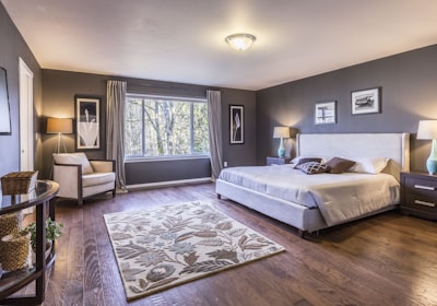 A large bedroom with the bed against the far wall, a patterned rug and two armchairs by the window