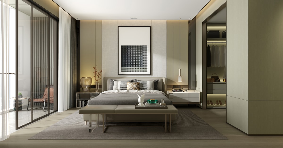 A bedroom in muted greens and creams, with a bench at the foot of the bed and framed art above it