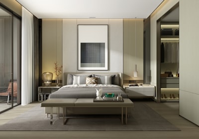 A bedroom in muted greens and creams, with a bench at the foot of the bed and framed art above it