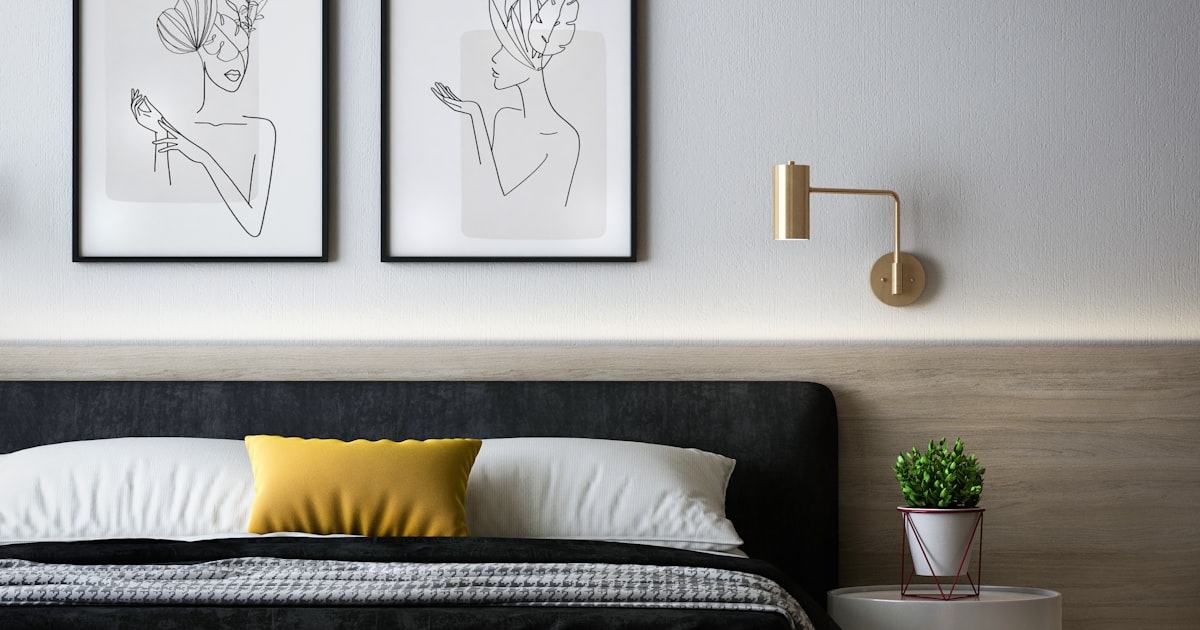 A bed with a dark headboard, two framed line drawings above it and a yellow cushion