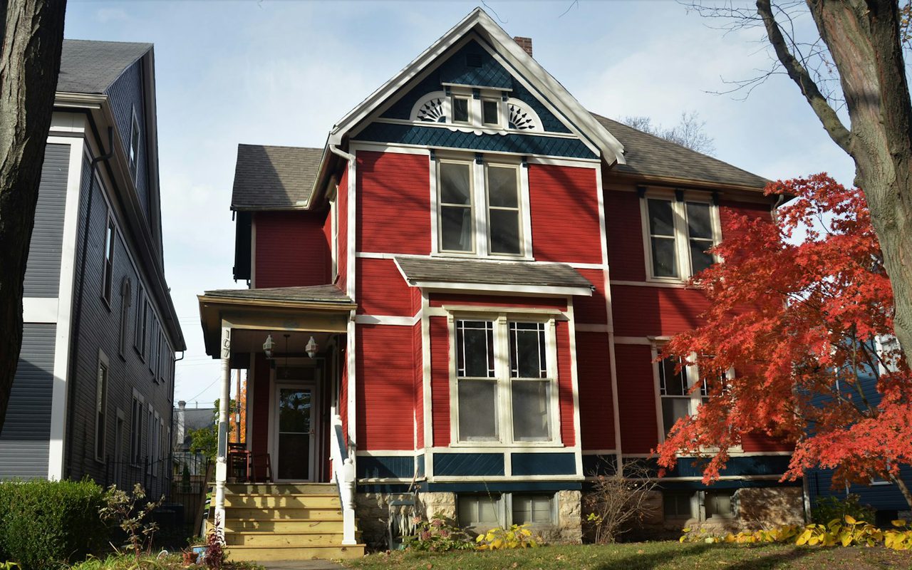 A red and white two story house with a covered front porch, seen from the street