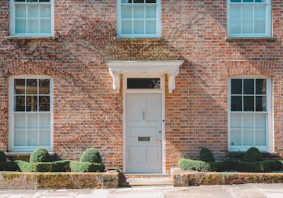 A red brick house with a pale front door, sash windows and clipped hedges either side of the path