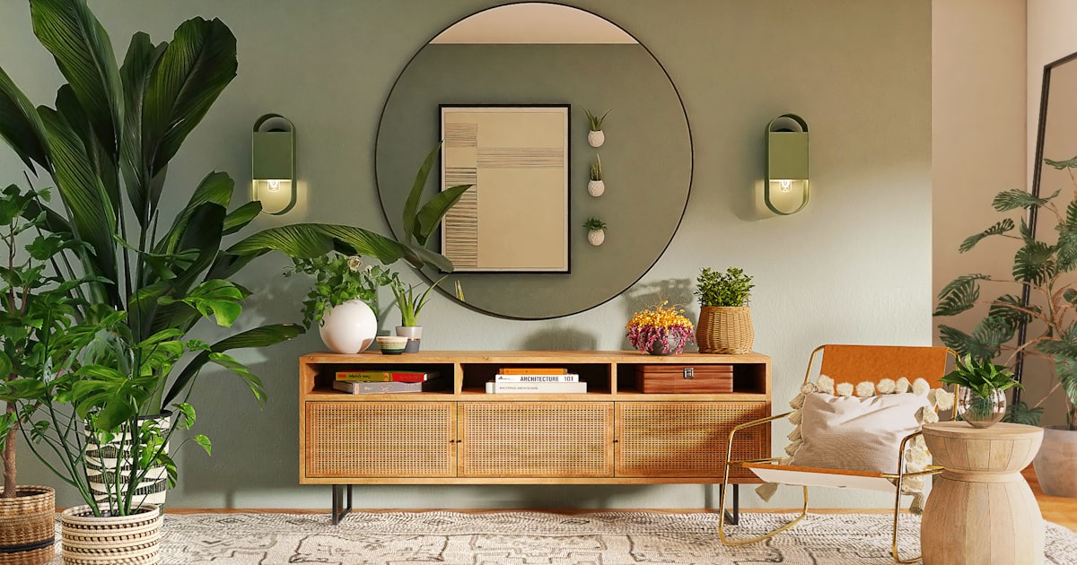 A green walled living space with large leafy plants, a round mirror and a wooden sideboard