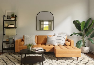 A tan sofa against a wall, with an arched mirror, open shelving and a large plant