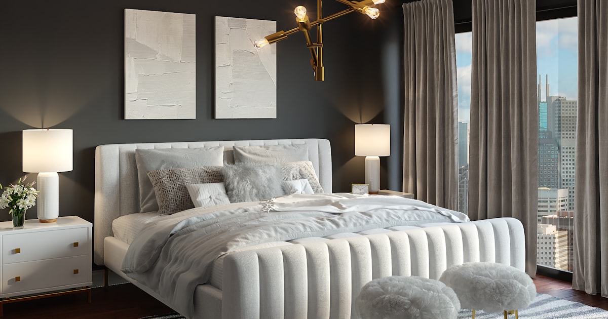 A gray bedroom with an upholstered double bed, a matching lamp on each side and a city window
