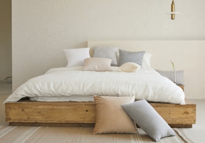 A low wooden platform bed with white bedding against a plain neutral wall