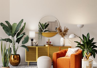A living room filled with potted plants, an orange armchair and a gold sideboard under a round mirror