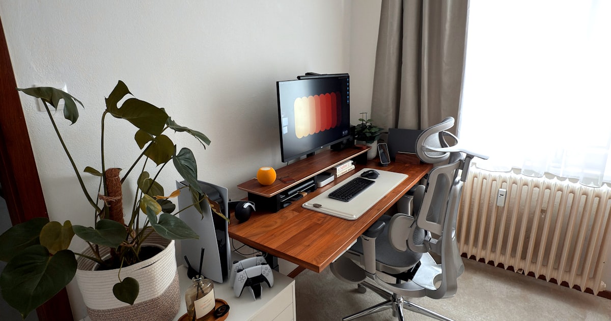 A desk with a monitor and keyboard, an office chair and a trailing plant beside the window